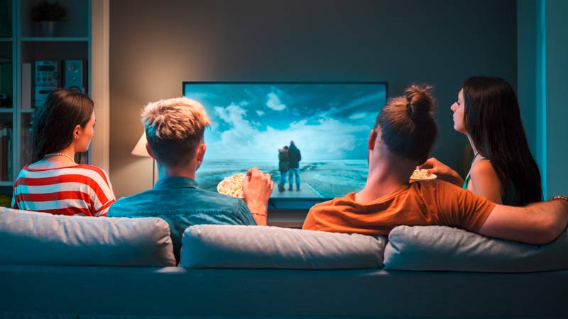 grupo de quatro amigos a ver televisão numa sala, sentados no sofá